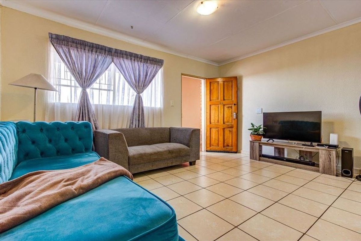 A living room featuring ceramic floor tiles, a wooden door, and a window with security bars.