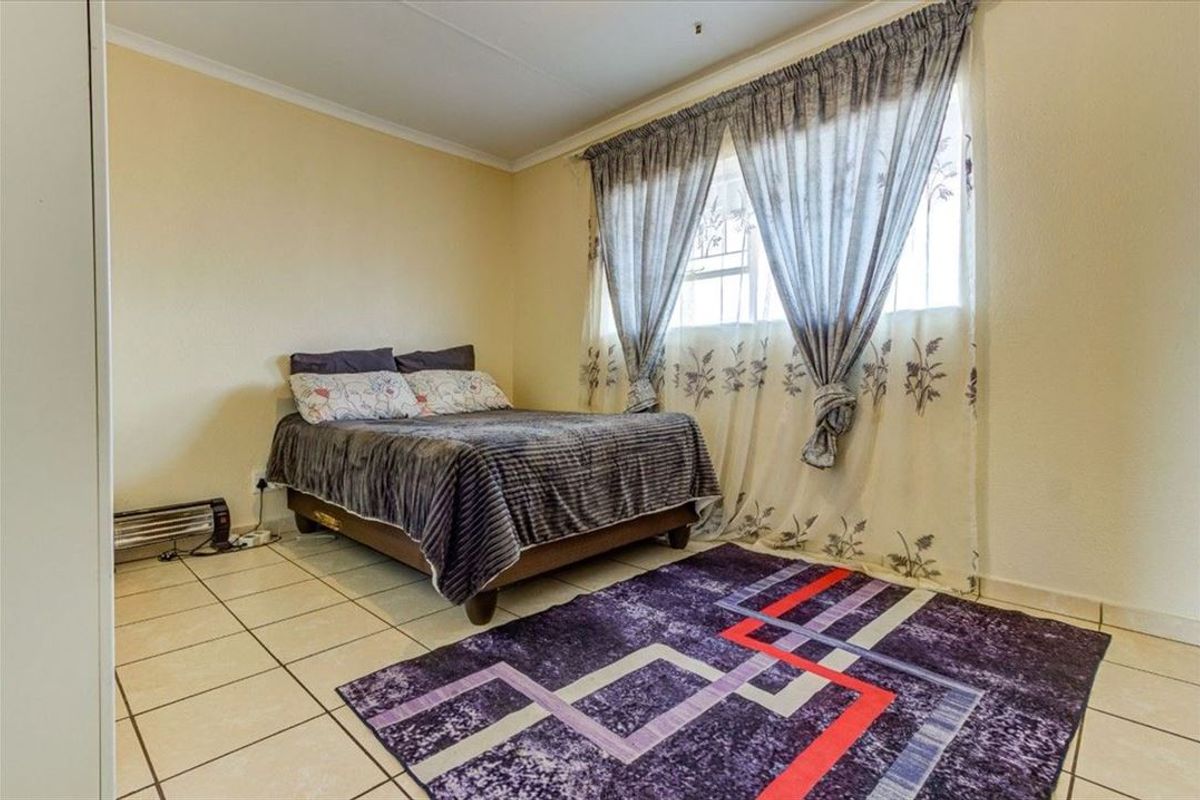 A functional bedroom featuring tiled flooring and a window with security bars, providing a simple and practical living space.