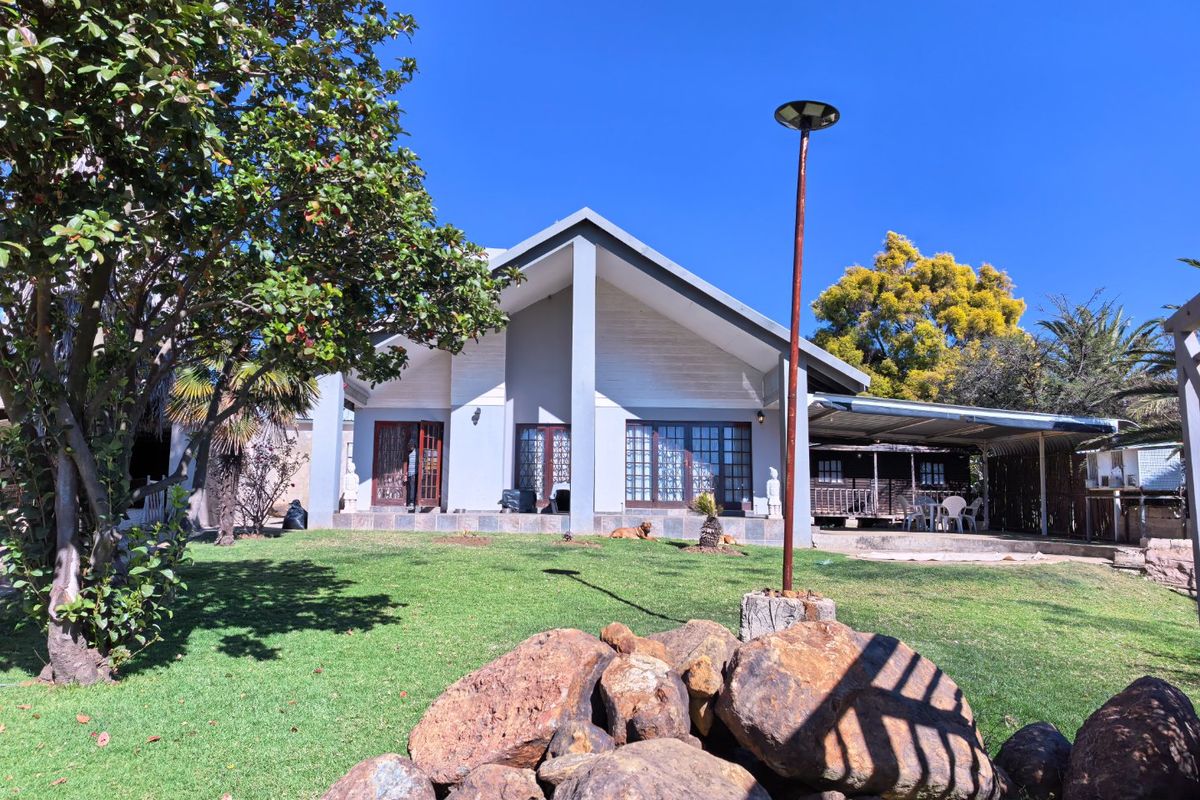 A view of the rear exterior of the house featuring a gabled roofline, covered patio area, and a spacious landscaped garden.