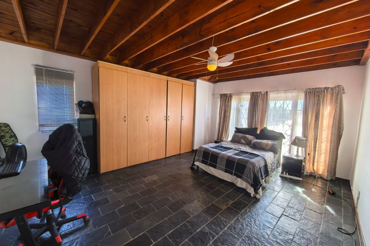Spacious bedroom featuring exposed timber beam ceilings, slate tile flooring, and extensive built-in wooden cabinetry.