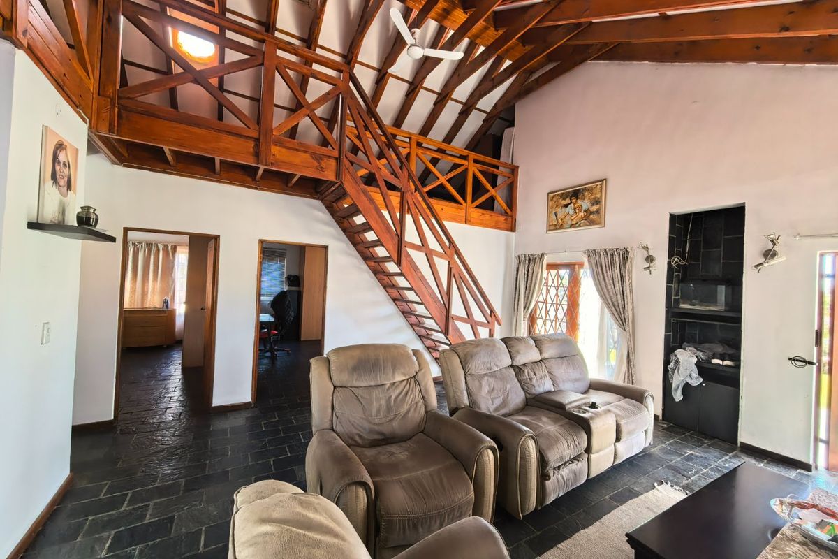 Spacious living area featuring a double-volume vaulted timber ceiling, a mezzanine level with wooden staircase, and dark slate flooring.