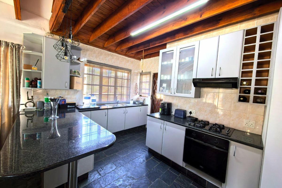 Spacious kitchen featuring granite countertops, built-in oven and hob, exposed timber ceiling beams, and slate flooring with ample cabinetry and a breakfast bar.