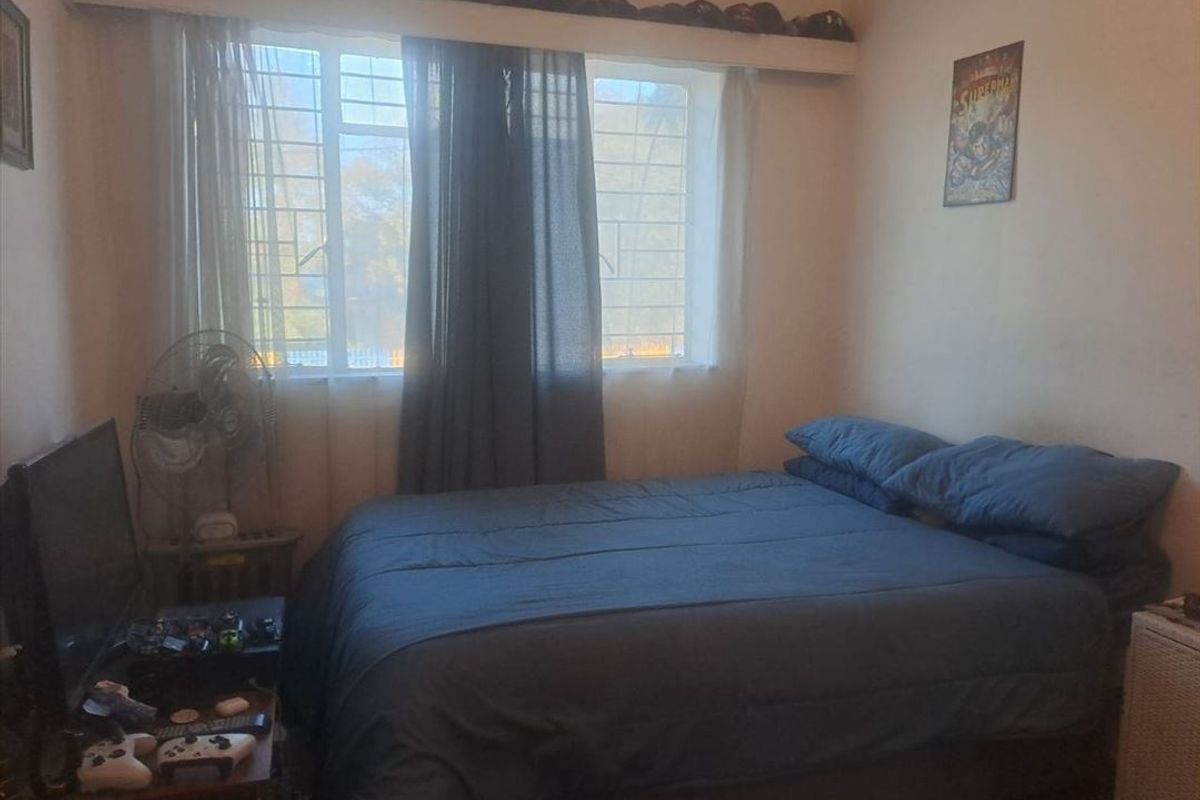 A functional bedroom featuring a large window with security bars, providing natural light and a view of the exterior.