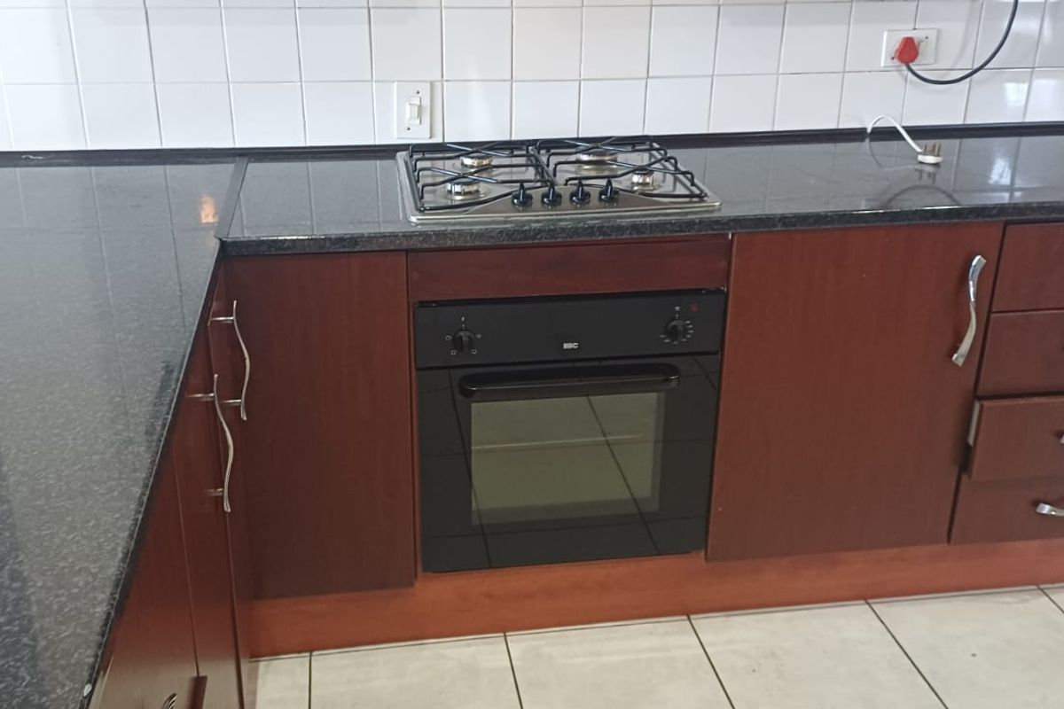 A functional kitchen featuring dark granite countertops, wooden cabinetry, a built-in oven, and a gas hob with white tiled splashbacks.
