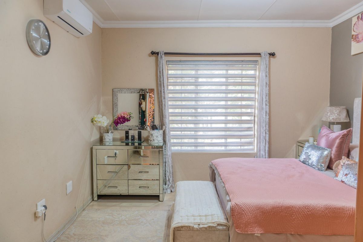 A bedroom featuring a wall-mounted air conditioning unit, a window with fitted blinds, and neutral wall finishes.