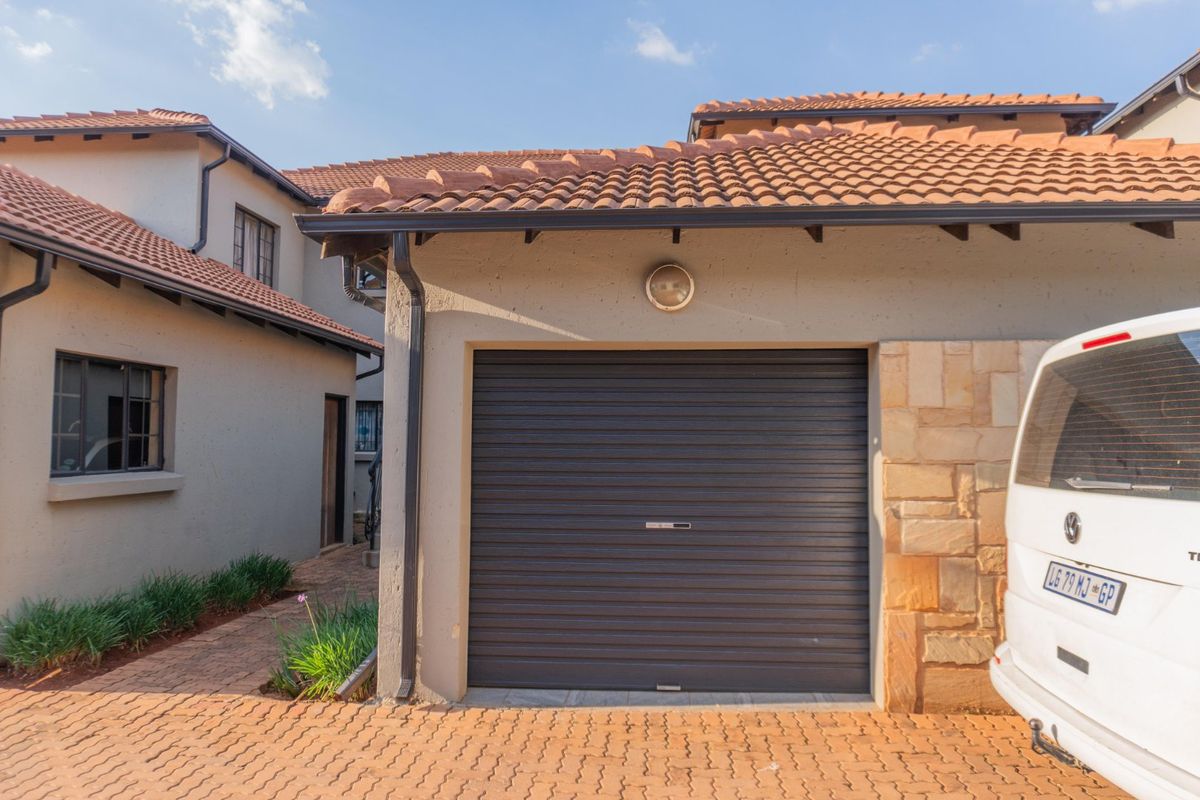 Exterior view of the property featuring a single garage with a roller door, tiled roof, and paved driveway.