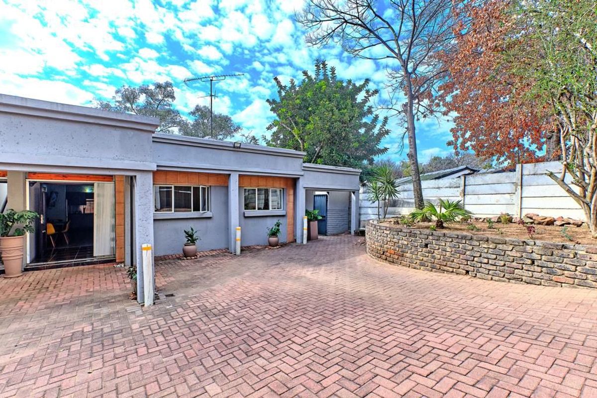 A paved courtyard area featuring a brick retaining wall, mature trees, and direct access to the apartment interior.