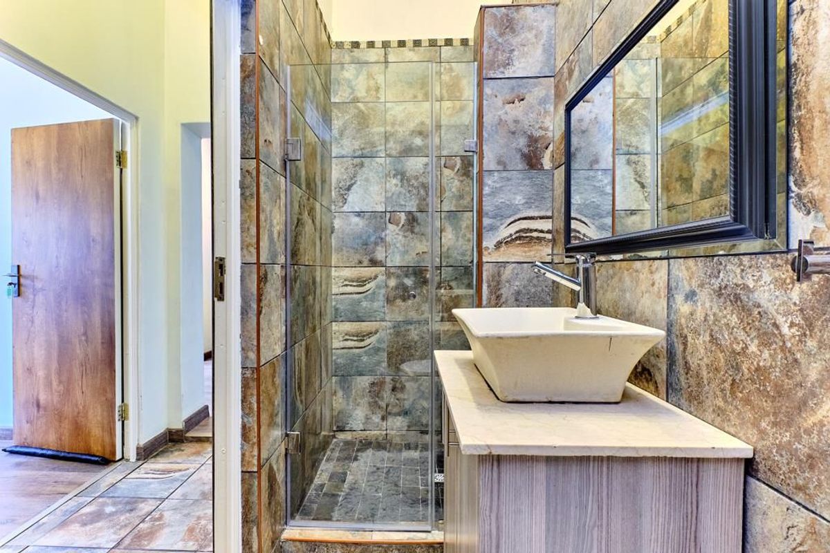 A bathroom featuring a walk-in shower with stone-look wall tiles, a vessel sink mounted on a vanity cabinet, and a framed wall mirror.