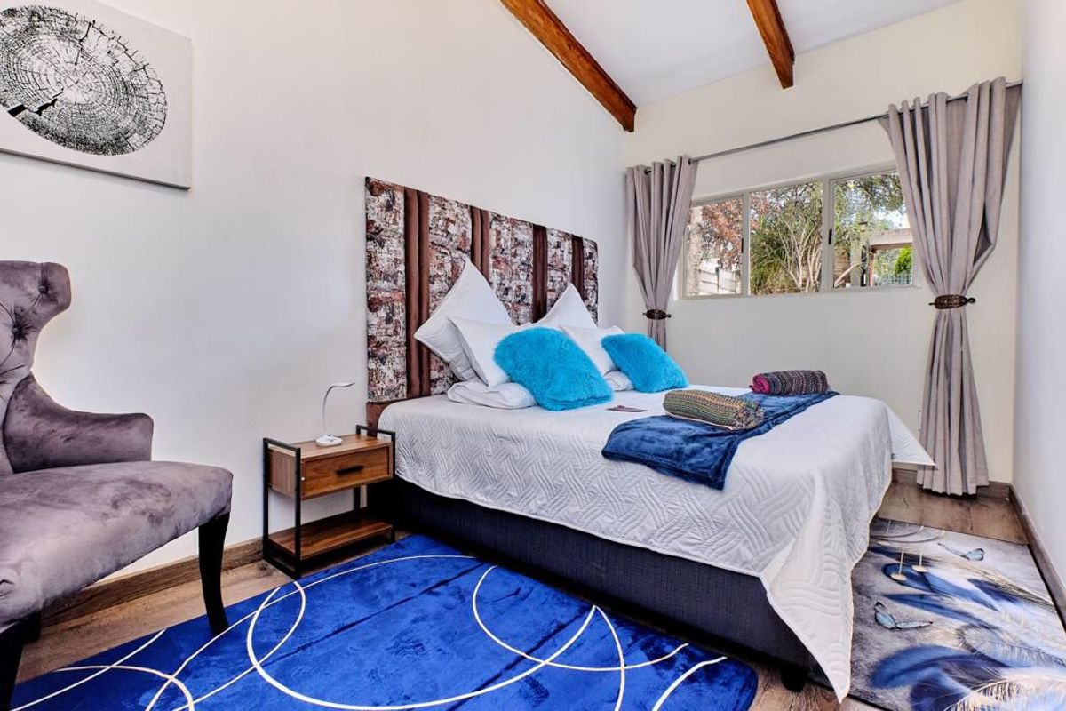 A well-lit bedroom featuring exposed wooden ceiling beams, laminate flooring, and a large window providing natural light.