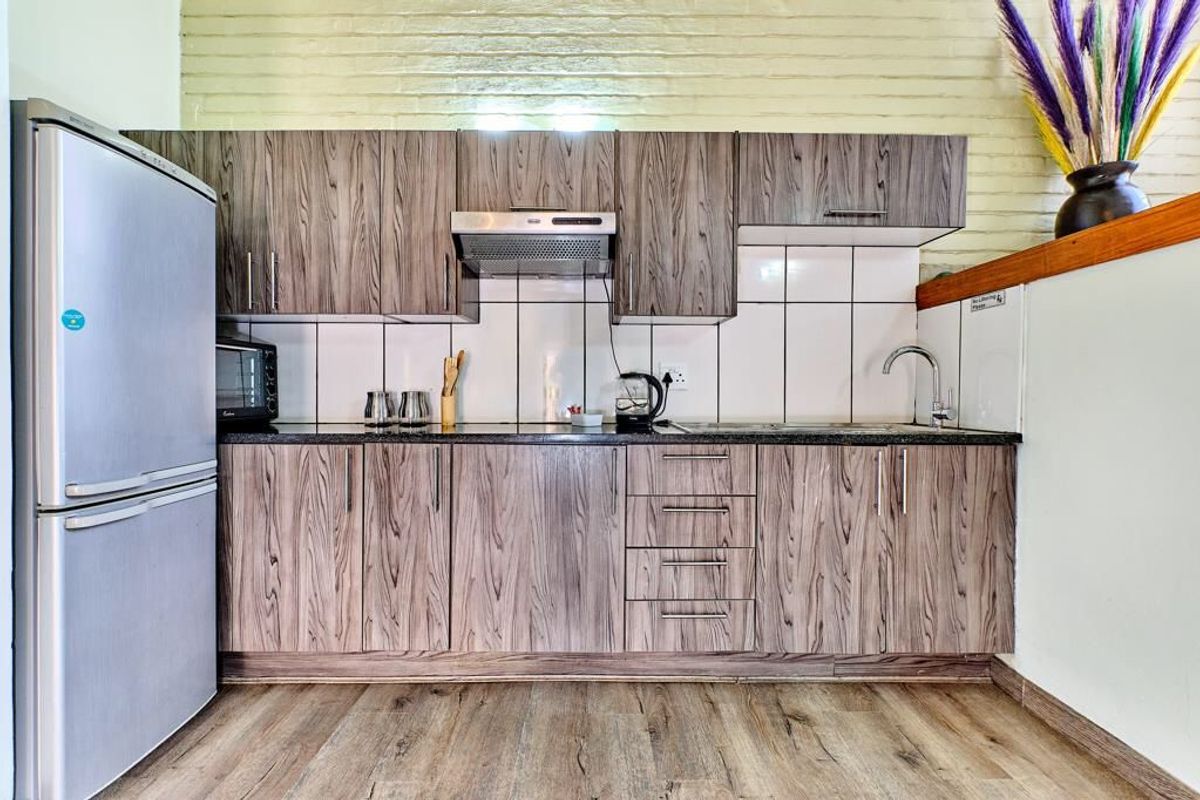 Compact kitchen featuring wood-grain cabinetry, dark countertops, tiled backsplash, and built-in extractor fan, set against a textured brick wall.