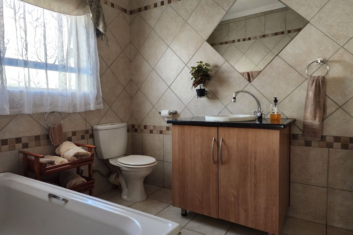 A functional bathroom featuring a vanity cabinet with a granite countertop, a standard toilet, and a bathtub with tiled walls.