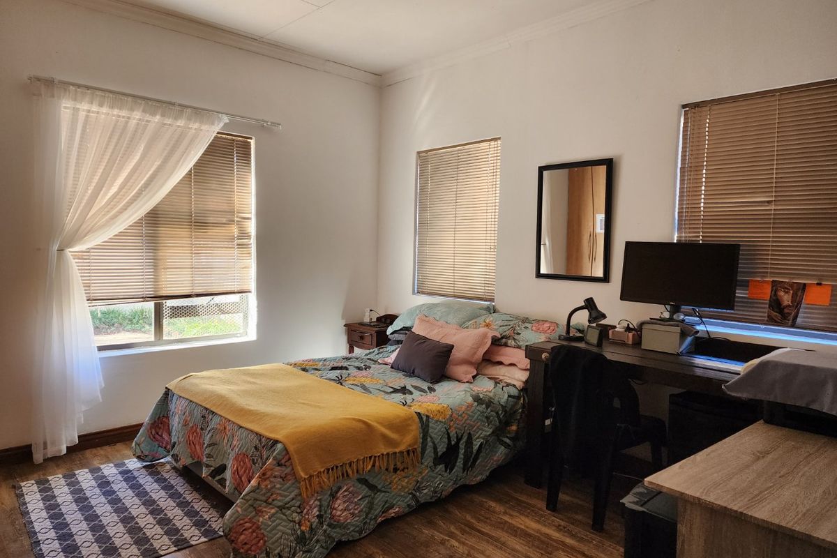 A well-lit bedroom featuring wood-look flooring, multiple windows with fitted blinds, and neutral wall finishes.