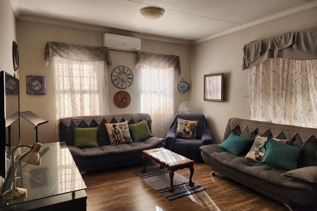 A comfortable living room featuring wood-look flooring, multiple windows with valance curtains, and a wall-mounted air conditioning unit.