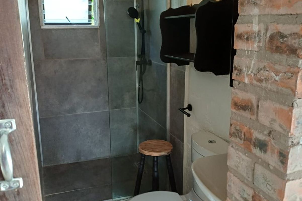 Compact bathroom featuring a glass-enclosed shower, modern grey floor-to-ceiling tiling, a standard toilet, and a vanity unit.