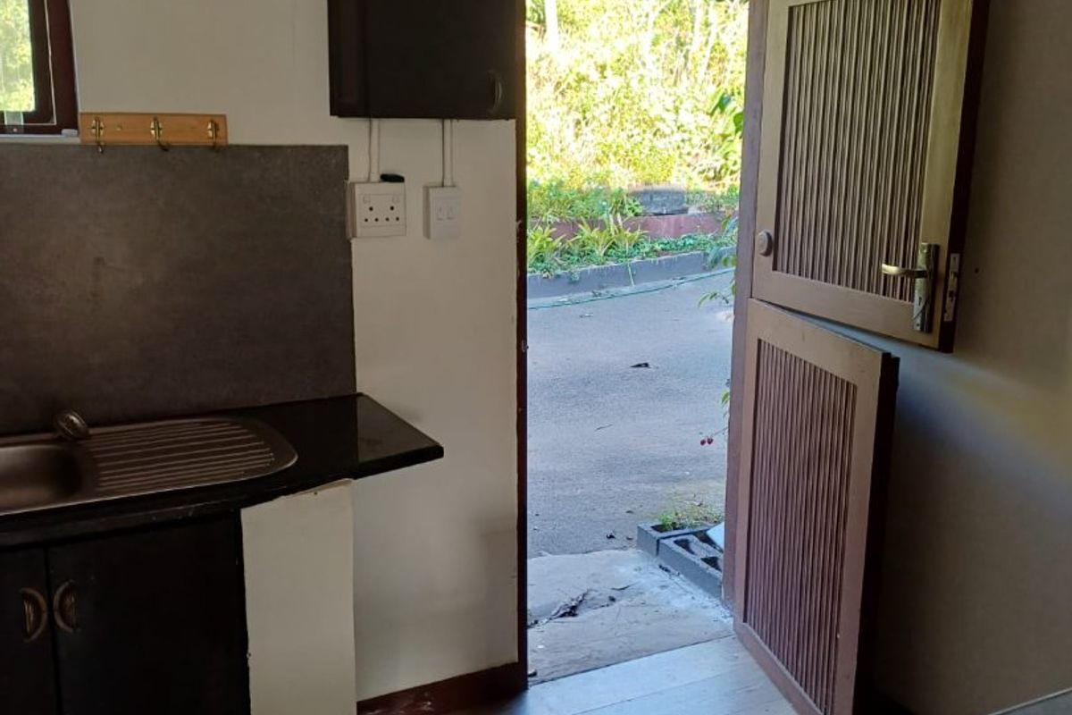 A functional kitchen area featuring dark cabinetry, a stainless steel sink, and direct access to the exterior through a stable-style door.