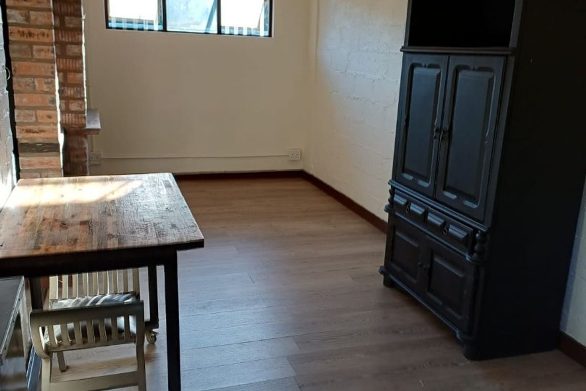 A living area featuring wood-look laminate flooring, a brick feature pillar, and a high-gloss ceiling finish with a classic chandelier.