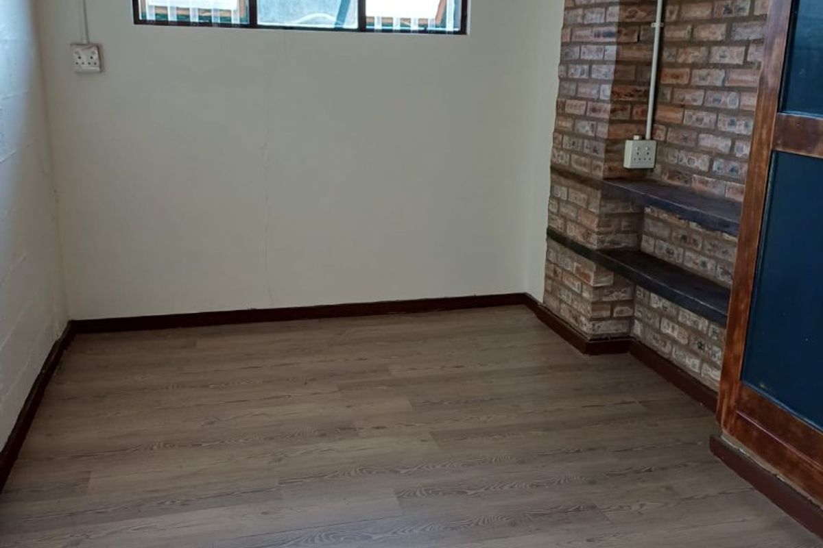 A bedroom featuring wood-look laminate flooring, a brick feature wall with built-in shelving, and a window with security bars.