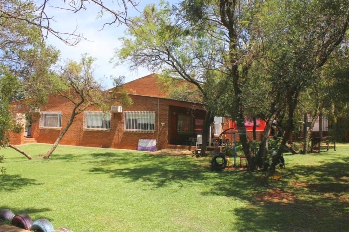 A view of the rear brick facade of the house, featuring a spacious garden area with mature trees and a covered patio.