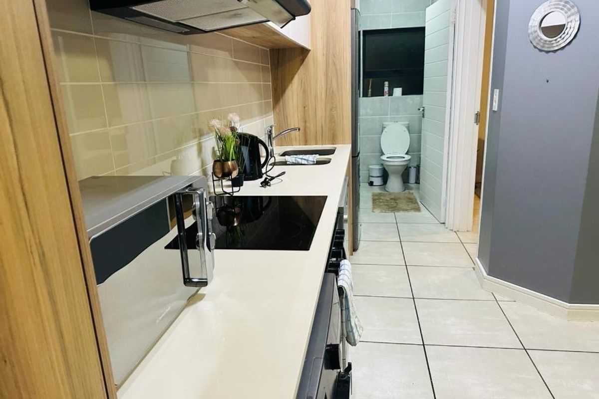 A compact kitchen featuring modern cabinetry, a built-in hob, and an extractor fan, with an adjacent bathroom visible through the doorway.