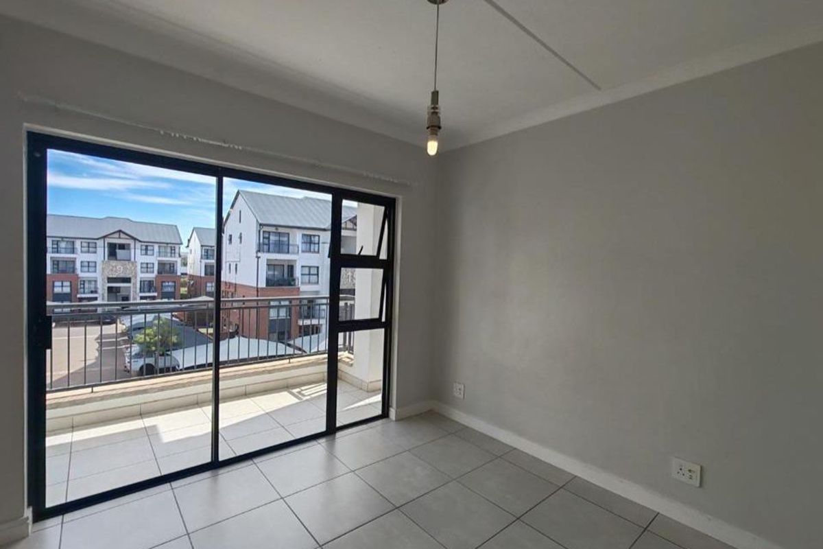 Bright living area featuring large sliding glass doors that open onto a private balcony with tiled flooring and neutral wall finishes.