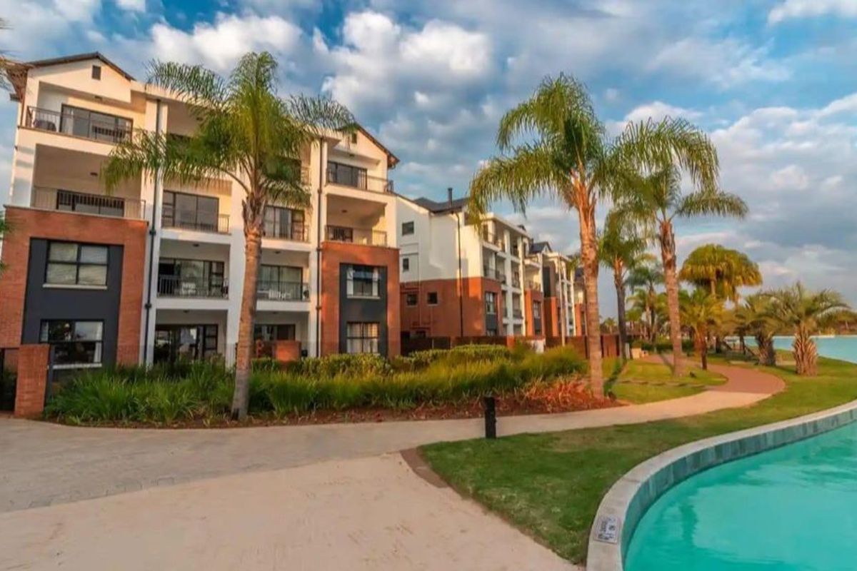 A view of the apartment complex exterior featuring modern brick and plaster facades, balconies, and landscaped grounds adjacent to a swimming pool.