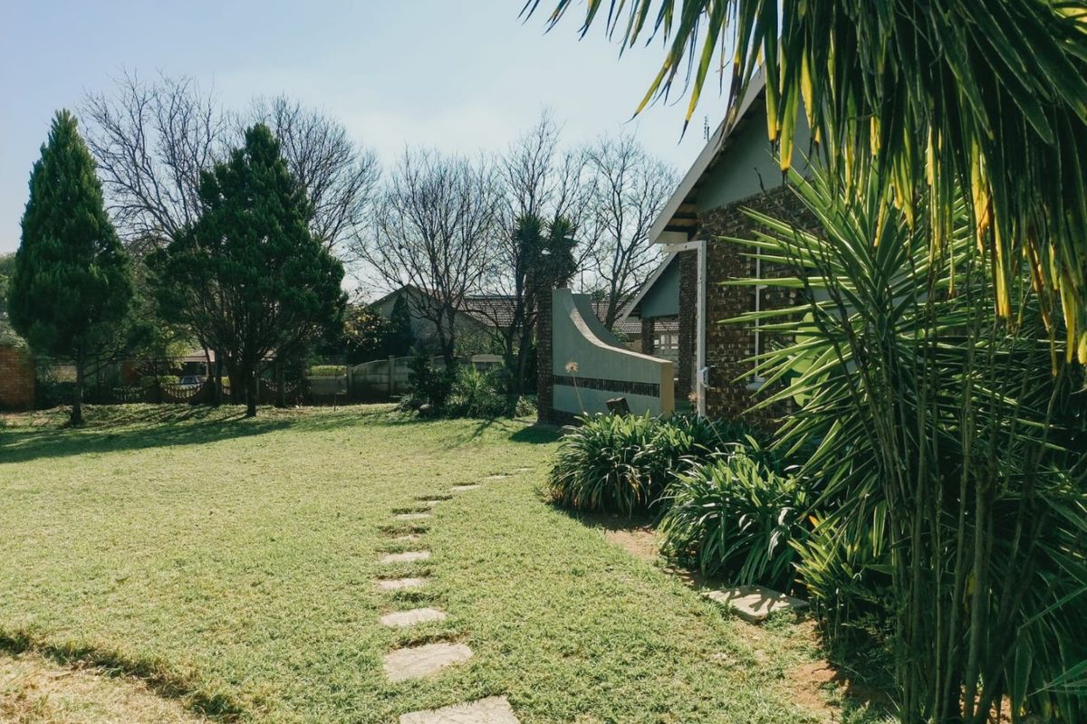 A spacious rear garden featuring a manicured lawn, established trees, and a stone pathway leading toward the side of the house.