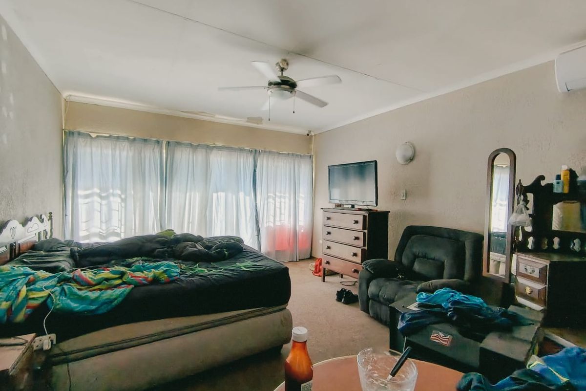 A bedroom featuring a ceiling fan, wall-mounted air conditioning unit, and large windows with curtains.