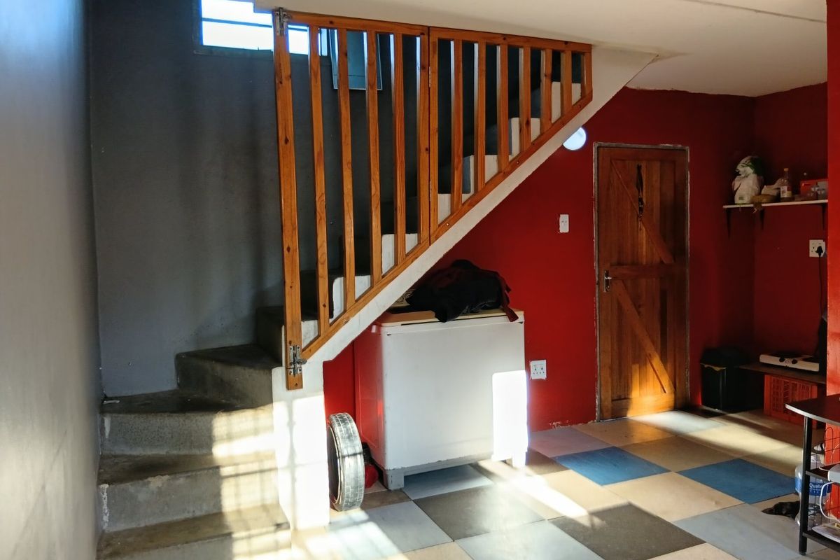 Interior view of a utility space featuring a concrete staircase with a wooden balustrade, tiled flooring, and a solid timber door.