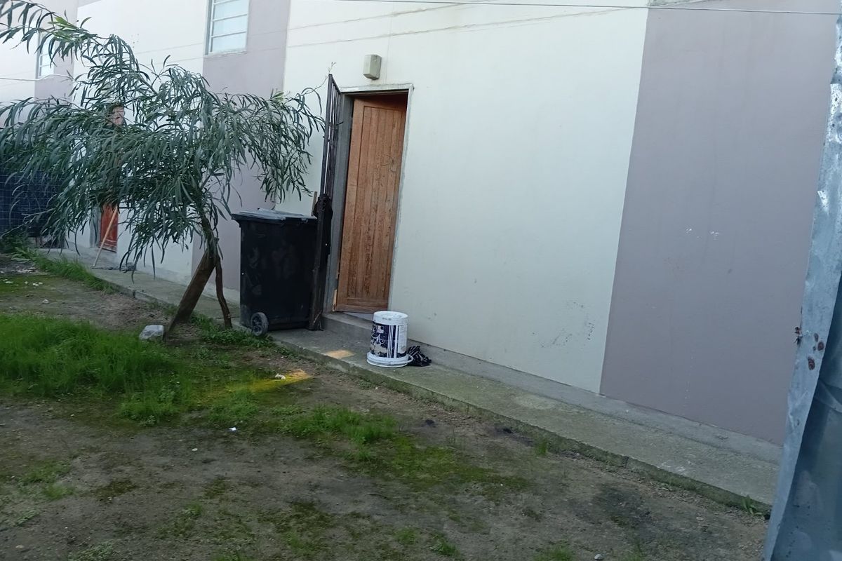 A view of the rear exterior of the property featuring a wooden door, concrete pathway, and a small garden area.
