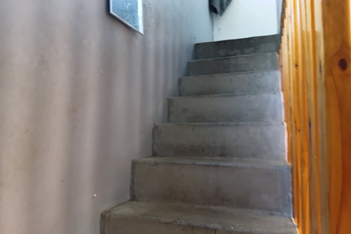 A simple staircase featuring raw concrete steps and a wooden balustrade, providing functional access between levels.
