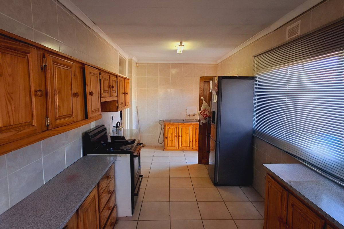 A functional kitchen featuring wooden cabinetry, tiled flooring, and wall-mounted tiling, offering a practical layout with ample storage and preparation space.