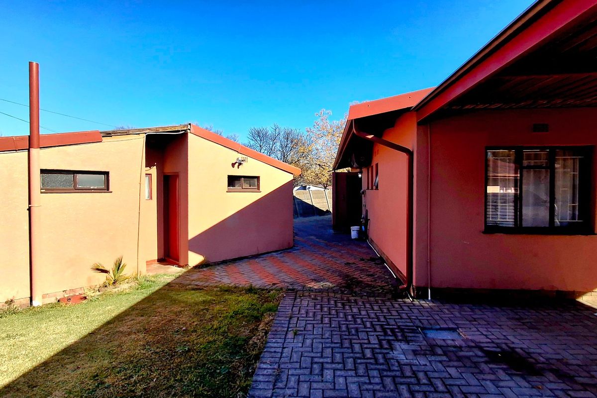 Exterior view of the property showing the rear courtyard area with paved pathways and access to outbuildings.