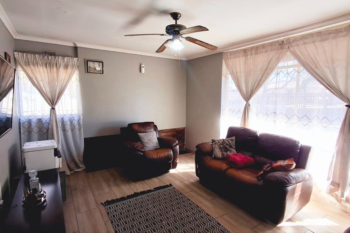A comfortable living room featuring tiled flooring, a ceiling fan, and large windows that provide ample natural light.