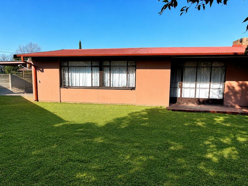 Rear view of the house featuring a corrugated metal roof, a timber deck, and a well-maintained lawn.