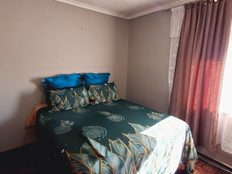 A standard bedroom featuring parquet flooring and natural light through a window with installed curtain rails.