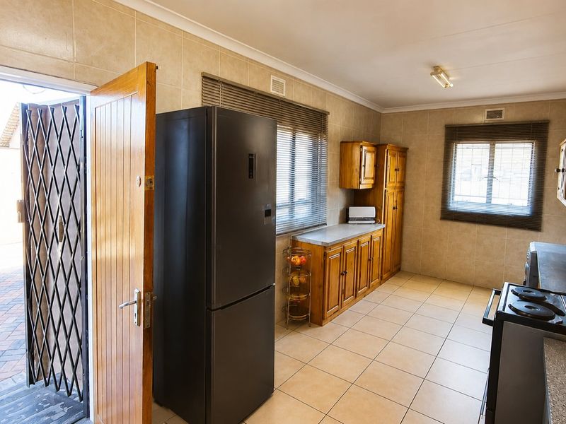 A functional kitchen featuring tiled walls and floors, wooden cabinetry, laminate countertops, and an electric stove, with direct access to an outdoor area.