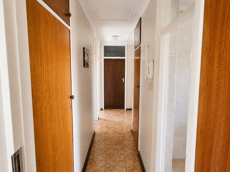 A functional hallway featuring tiled flooring, built-in wooden cupboards, and an intercom system, providing access to various rooms within the home.