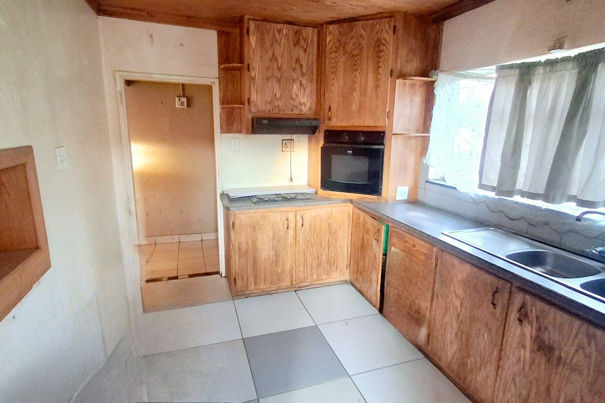 A dated kitchen featuring wood-veneer cabinetry, a built-in oven, extractor fan, and double-basin sink with tiled flooring.