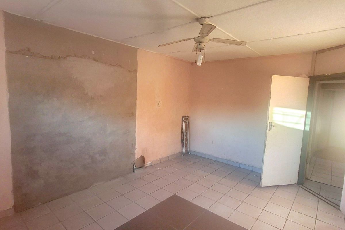 An empty room featuring tiled flooring, a ceiling fan, and walls requiring plaster repair and repainting.