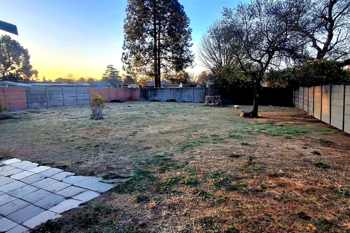 A spacious rear garden featuring a paved patio area, established trees, and perimeter boundary walls.