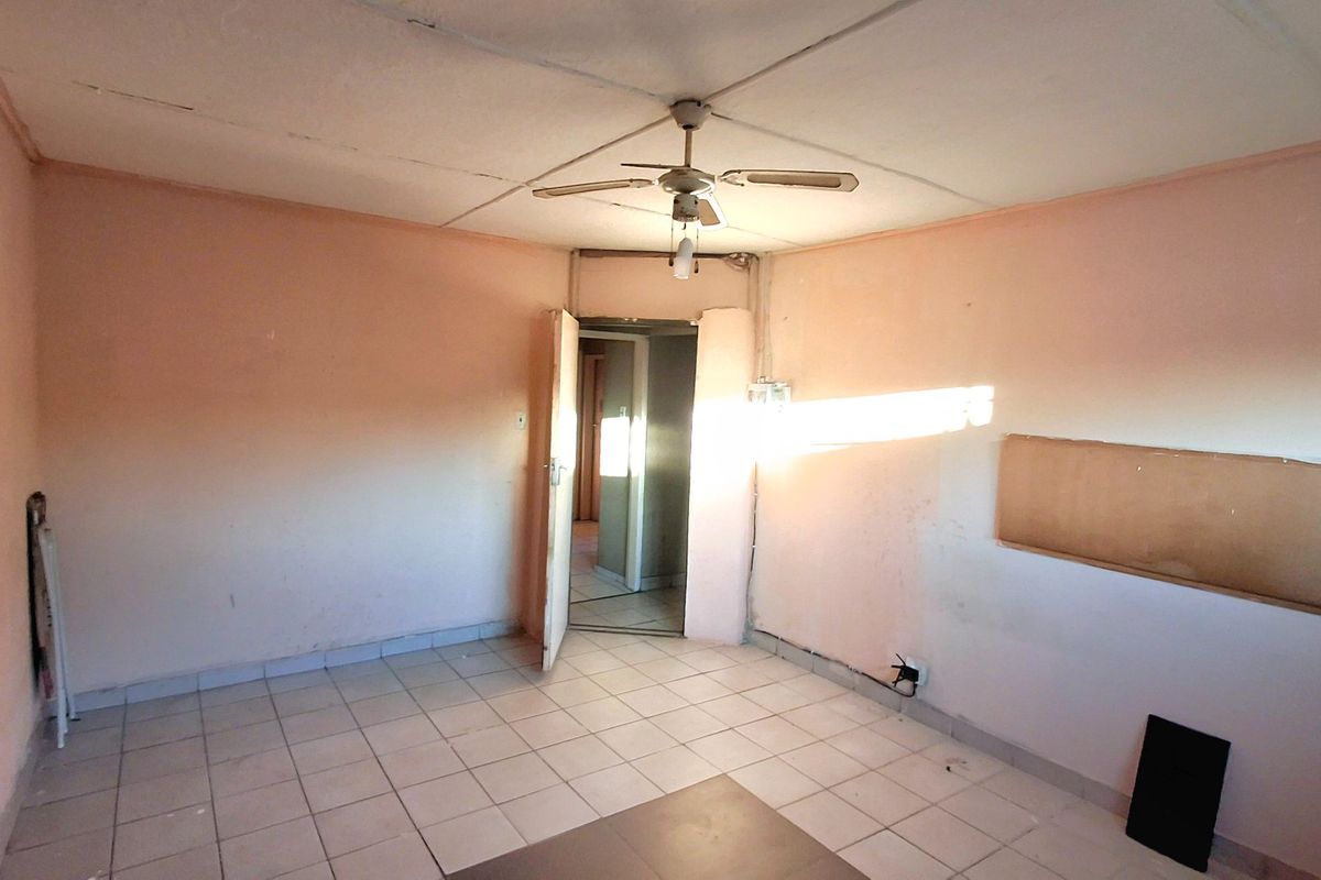 An empty room featuring tiled flooring, a ceiling fan, and a doorway leading to an adjacent hallway.