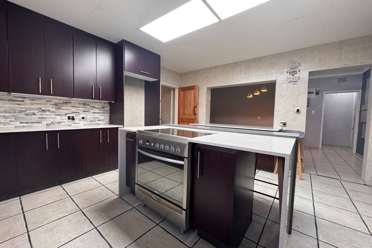 A functional kitchen featuring dark wood cabinetry, stone-look countertops, a central island with a built-in stove, and tiled flooring throughout.