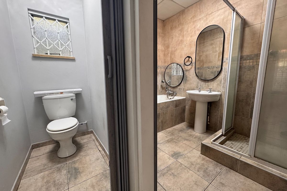 A combined bathroom and separate toilet area featuring a pedestal basin, bathtub, and glass-enclosed shower with neutral tiled finishes.