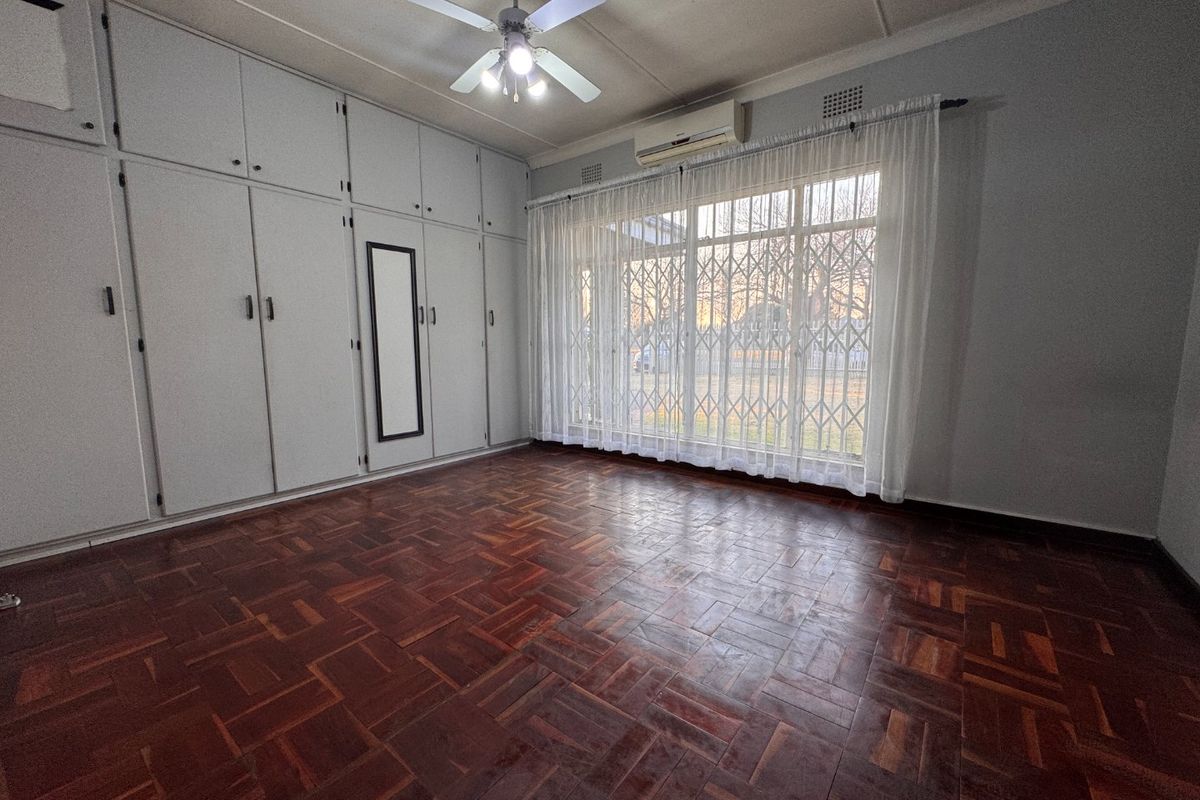 A spacious bedroom featuring classic parquet flooring, extensive built-in cabinetry, a ceiling fan, and a wall-mounted air conditioning unit.