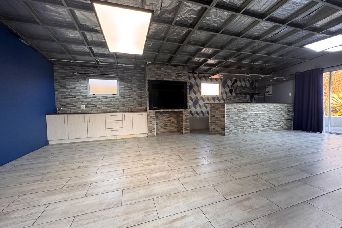 Spacious entertainment area featuring a built-in braai, stone-clad bar counter, cabinetry, and large format floor tiles, opening to an outdoor space.