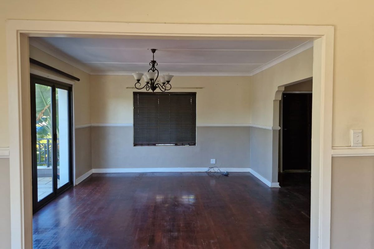 Spacious living area featuring dark timber flooring, neutral two-tone wall finishes, a decorative chandelier, and sliding glass doors leading to an outdoor space.