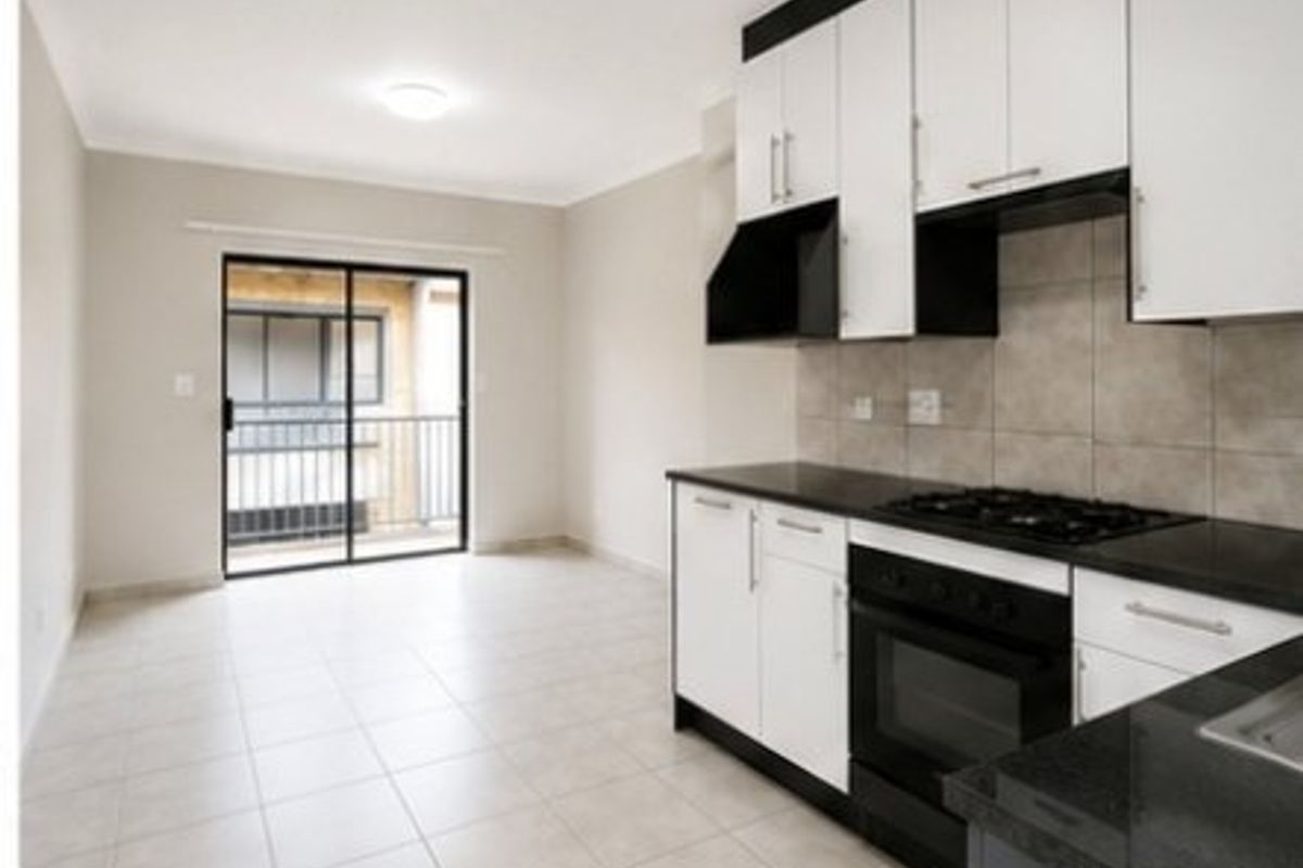 Open-plan kitchen and living area featuring modern white cabinetry, dark countertops, built-in oven and hob, and sliding glass doors leading to a balcony.