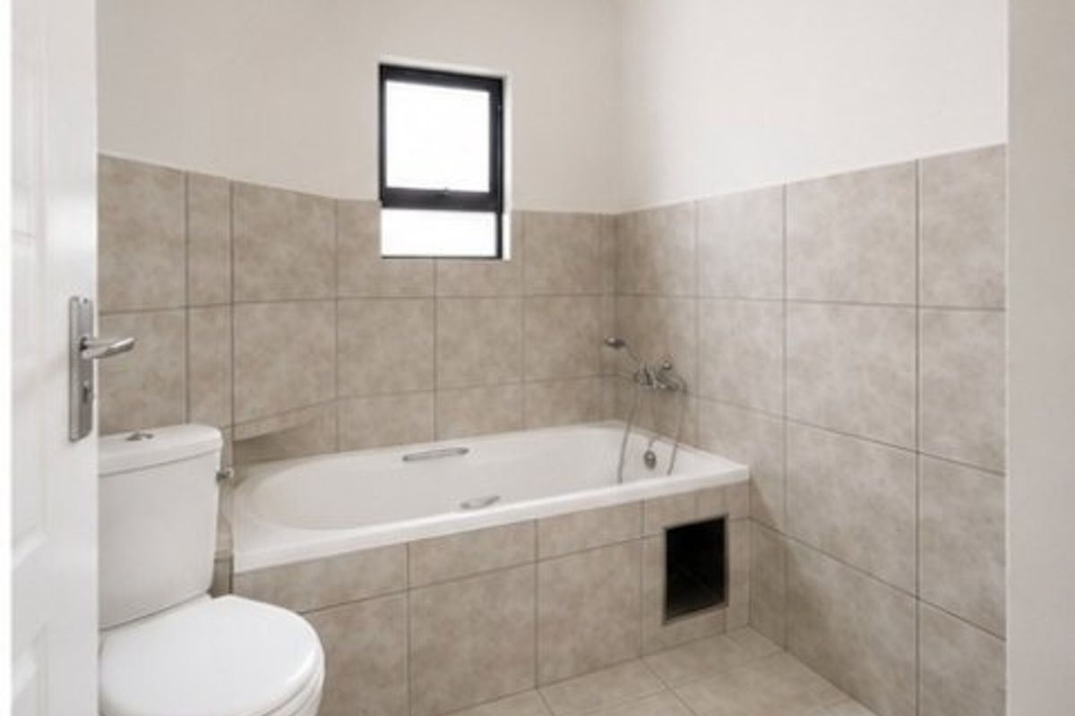 A functional bathroom featuring a built-in bathtub with shower mixer, tiled walls, and a standard toilet.