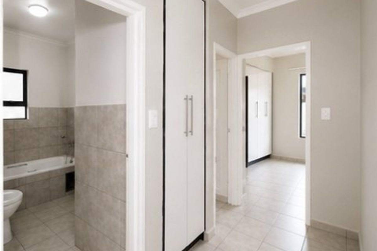 A bright hallway featuring neutral floor tiles, built-in storage cupboards, and direct access to a tiled bathroom and adjacent bedroom.