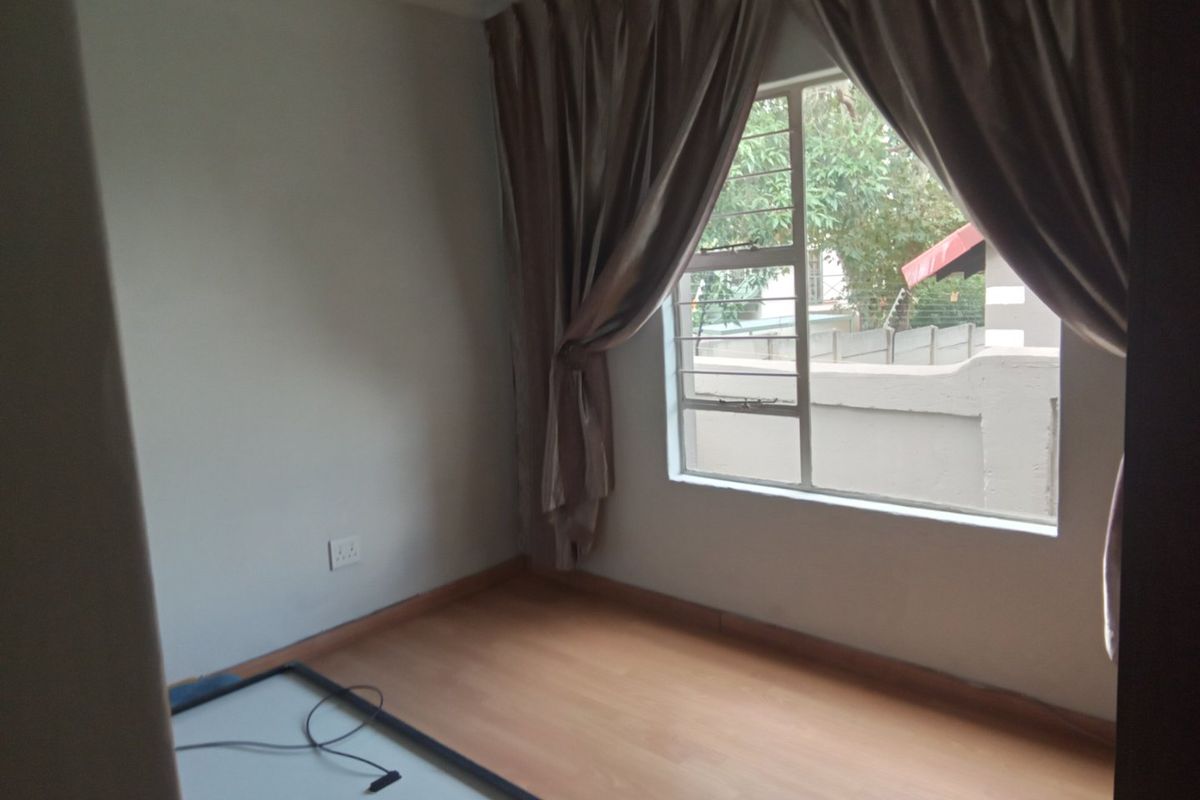 A bright, empty bedroom featuring laminate wood flooring, a large window with security bars, and neutral wall finishes.